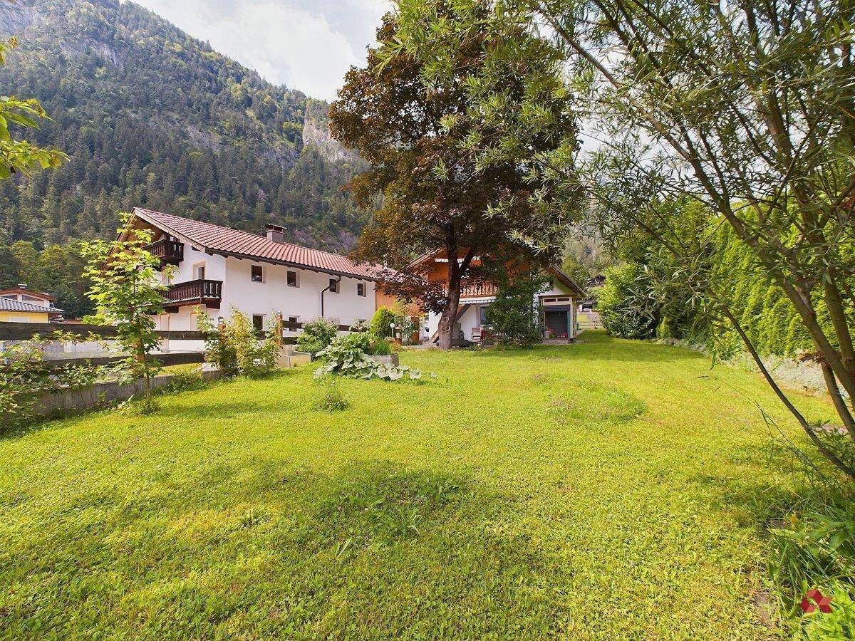Weitläufiger Garten mit Rasen und Bäumen, umgeben von einer natürlichen Berglandschaft.
