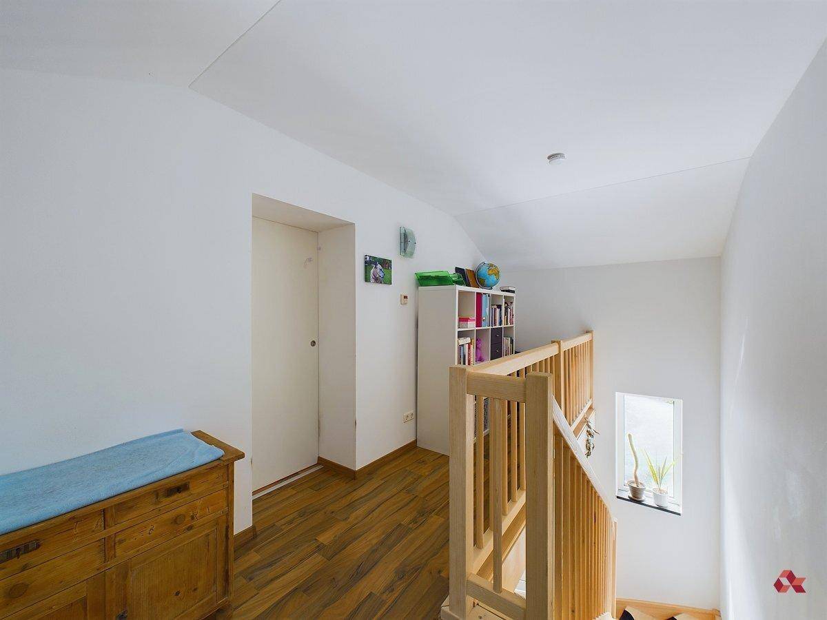 Heller Flur im Obergeschoss mit Holzgeländer, Holzboden und einem kleinen Fenster.