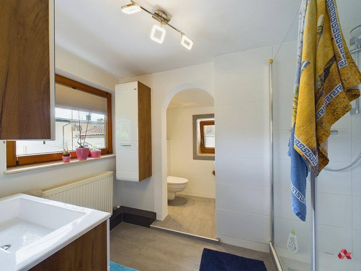 Modernes Badezimmer mit Dusche, Waschbecken und separatem WC-Bereich durch einen Bogen.