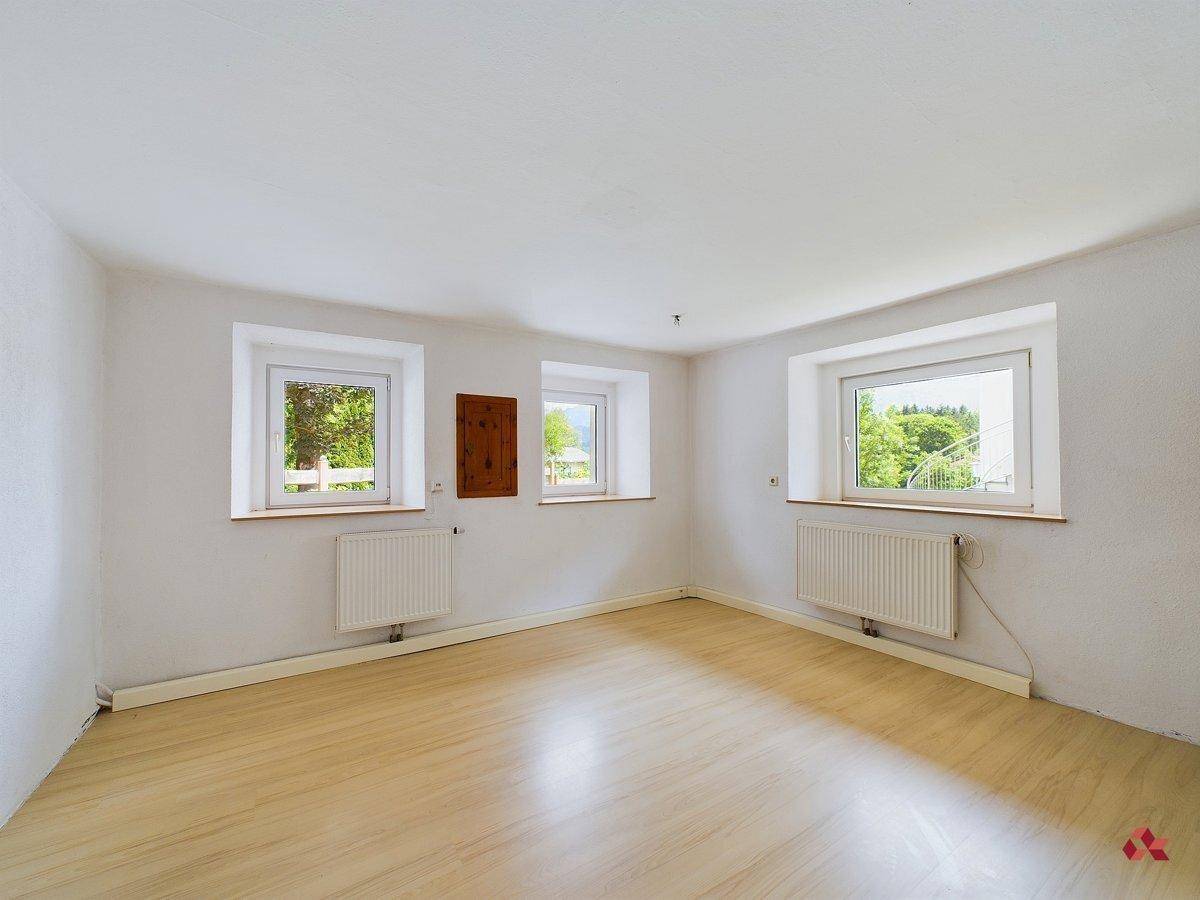 Geräumiger, heller Raum mit drei Fenstern und Laminatboden, ideal für Wohnzwecke.