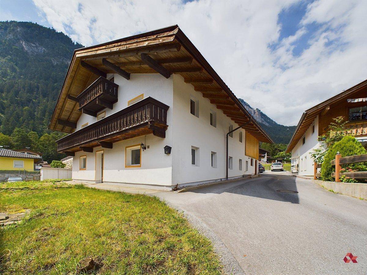 Traditionelles Haus mit weißer Fassade, Holzbalkonen und Satteldach in alpiner Umgebung.