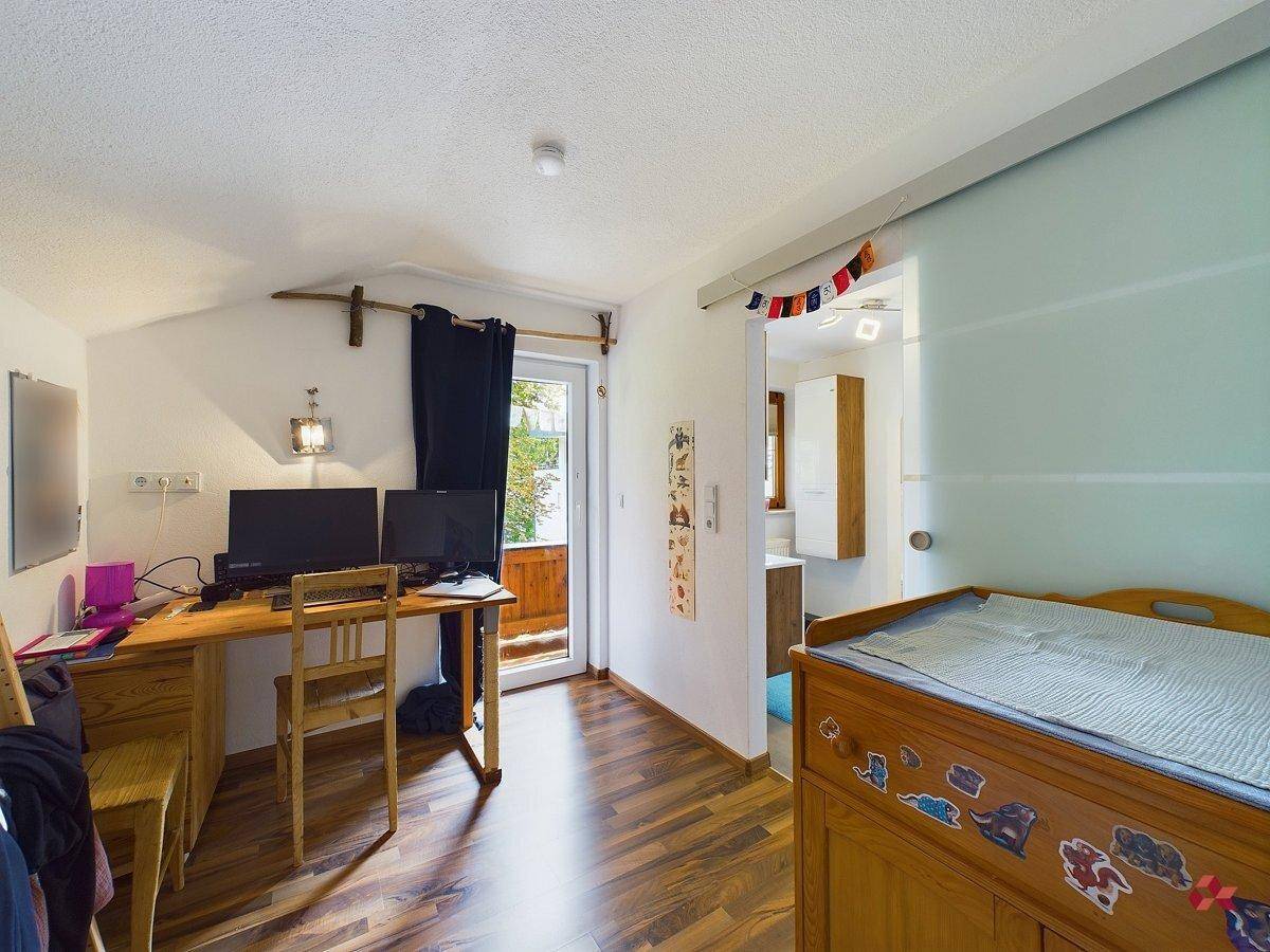 Helles Zimmer mit Holzboden, Schreibtisch und Zugang zu einem kleinen Balkon, ideal als Kinderzimmer.