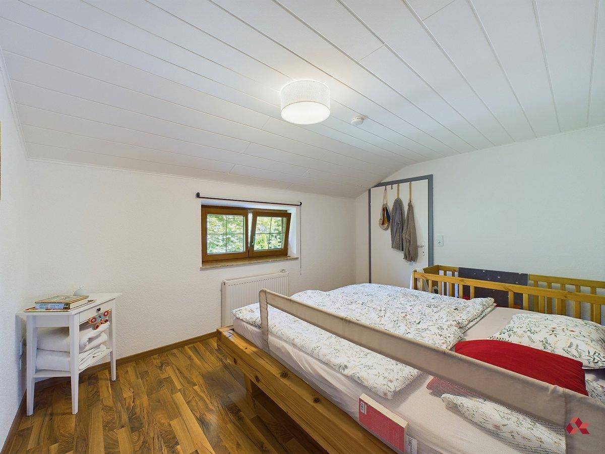 Gemütliches Schlafzimmer mit Holzboden, weißer Holzdecke und Fenster mit Blick ins Grüne.
