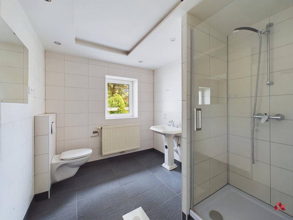 Geräumiges Badezimmer mit Duschkabine, Standwaschbecken und Fenster, ausgestattet mit dunklem Boden.