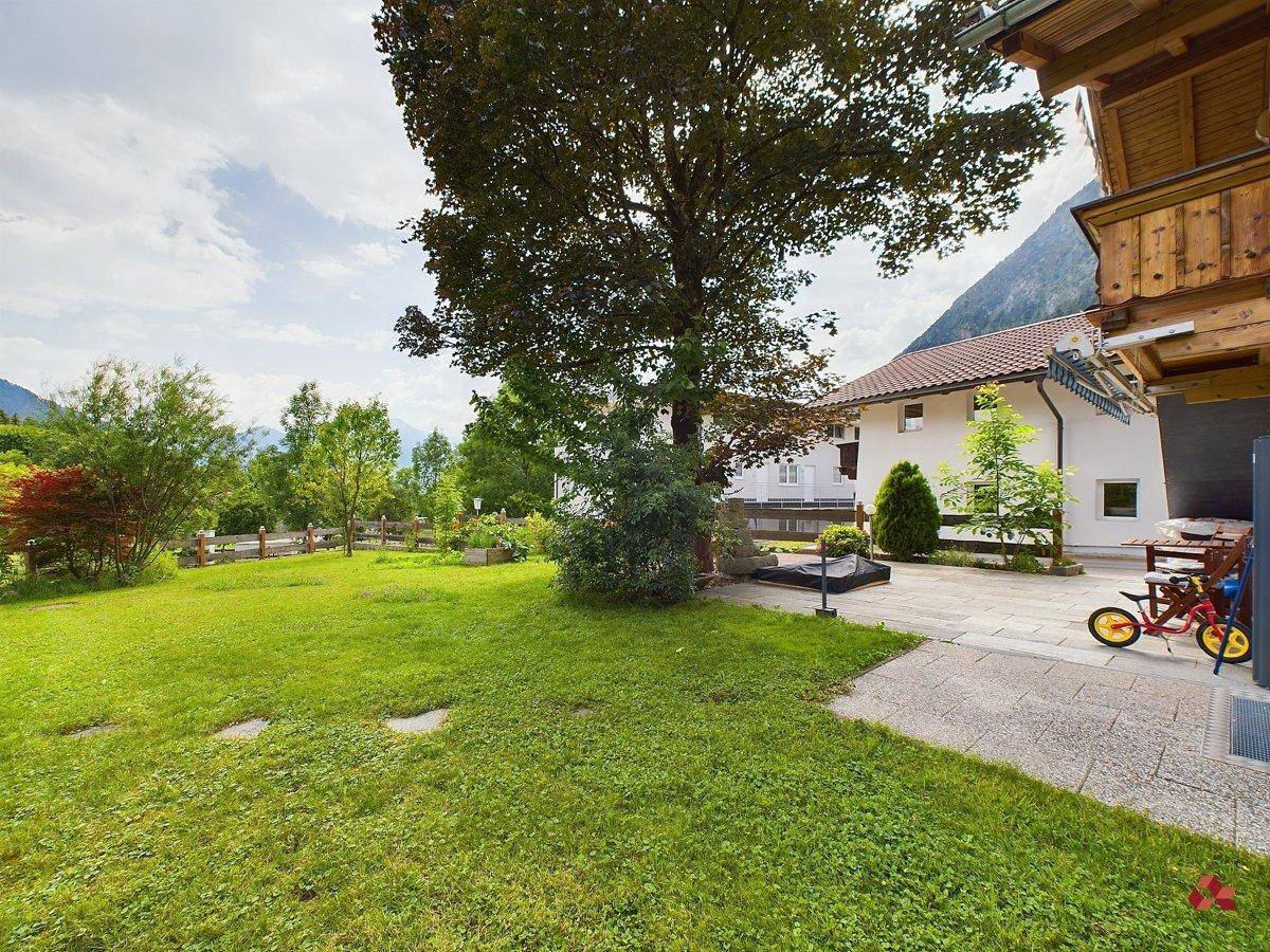Großer, gepflegter Garten mit Rasenfläche und altem Baum, umgeben von Bergen.