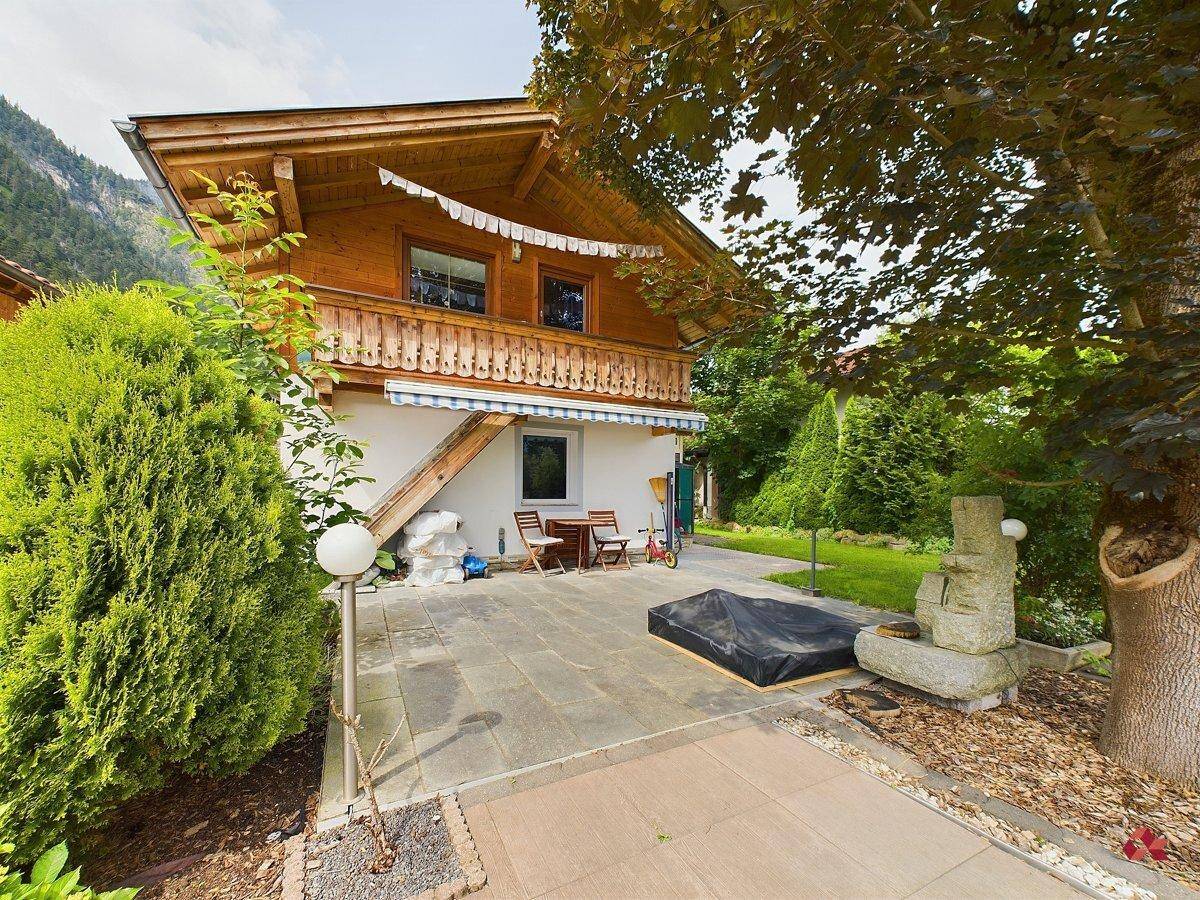 Gemütliche gepflasterte Terrasse neben dem Haus mit Holzbalkon und einem kleinen Brunnen.
