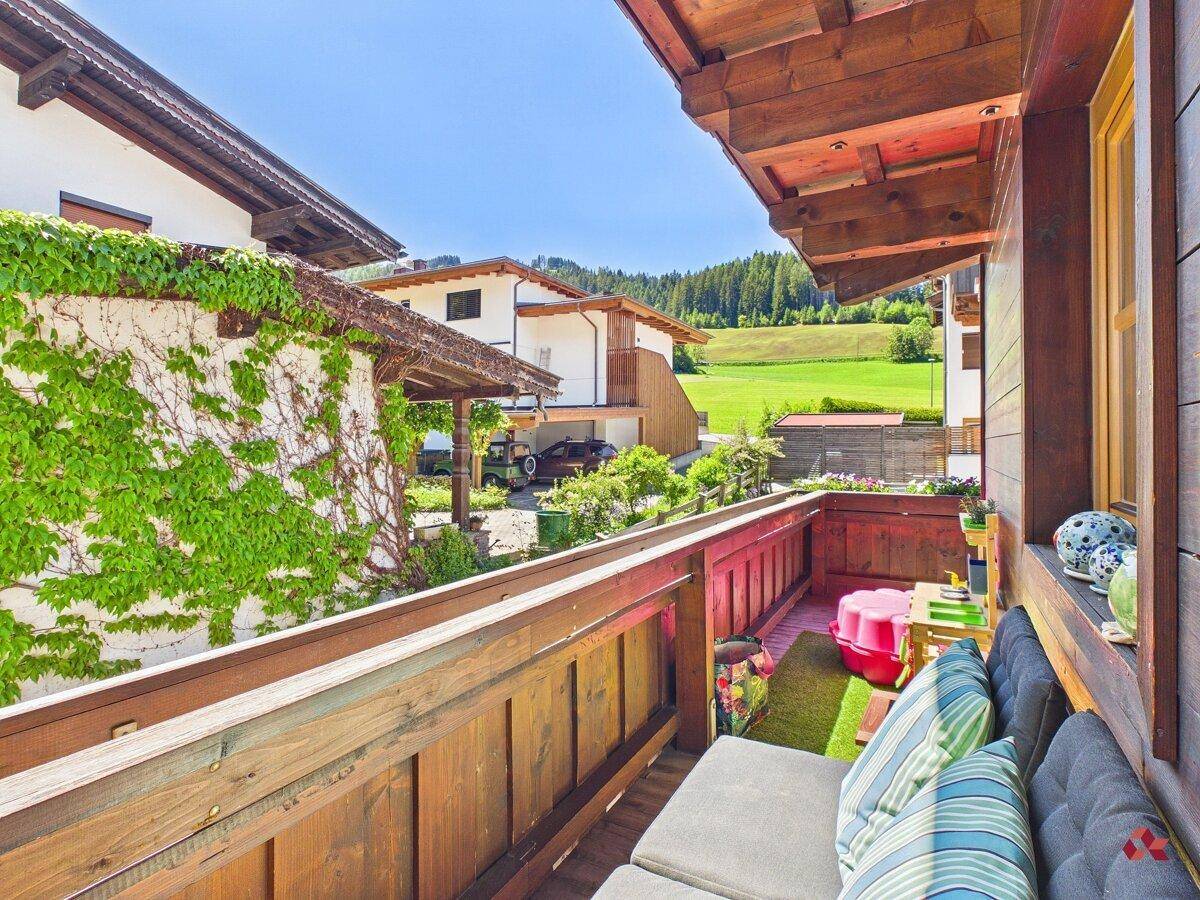 Sonniger Balkon mit Sitzgelegenheiten, Blumen und weitem Blick auf die ländliche Umgebung.