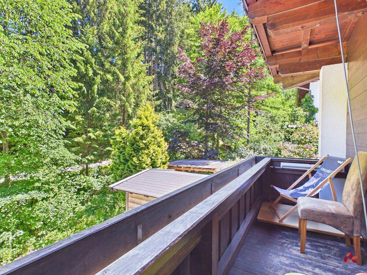Balkon mit Holzgeländer, Liegestuhl und einem schönen Blick auf den dichten Wald.