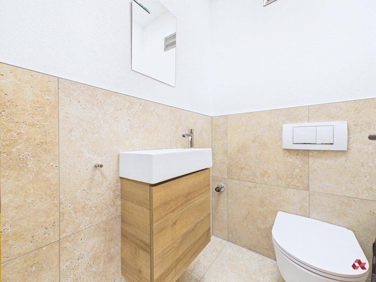 Modernes Gäste-WC mit Hänge-WC, kleinem Waschbecken und beigen Fliesen an den Wänden.