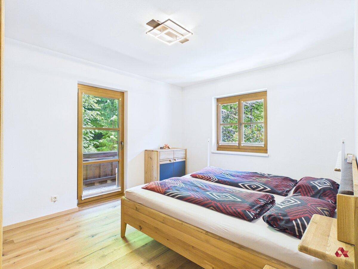 Gemütliches Schlafzimmer mit Holzbett, Parkettboden und Zugang zum Balkon mit Waldblick.
