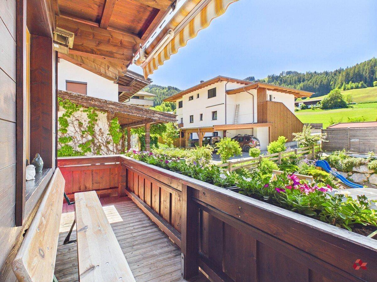 Sonniger Balkon mit Holzboden, Blumenkästen und weitem Blick auf die Landschaft und einen Spielplatz.