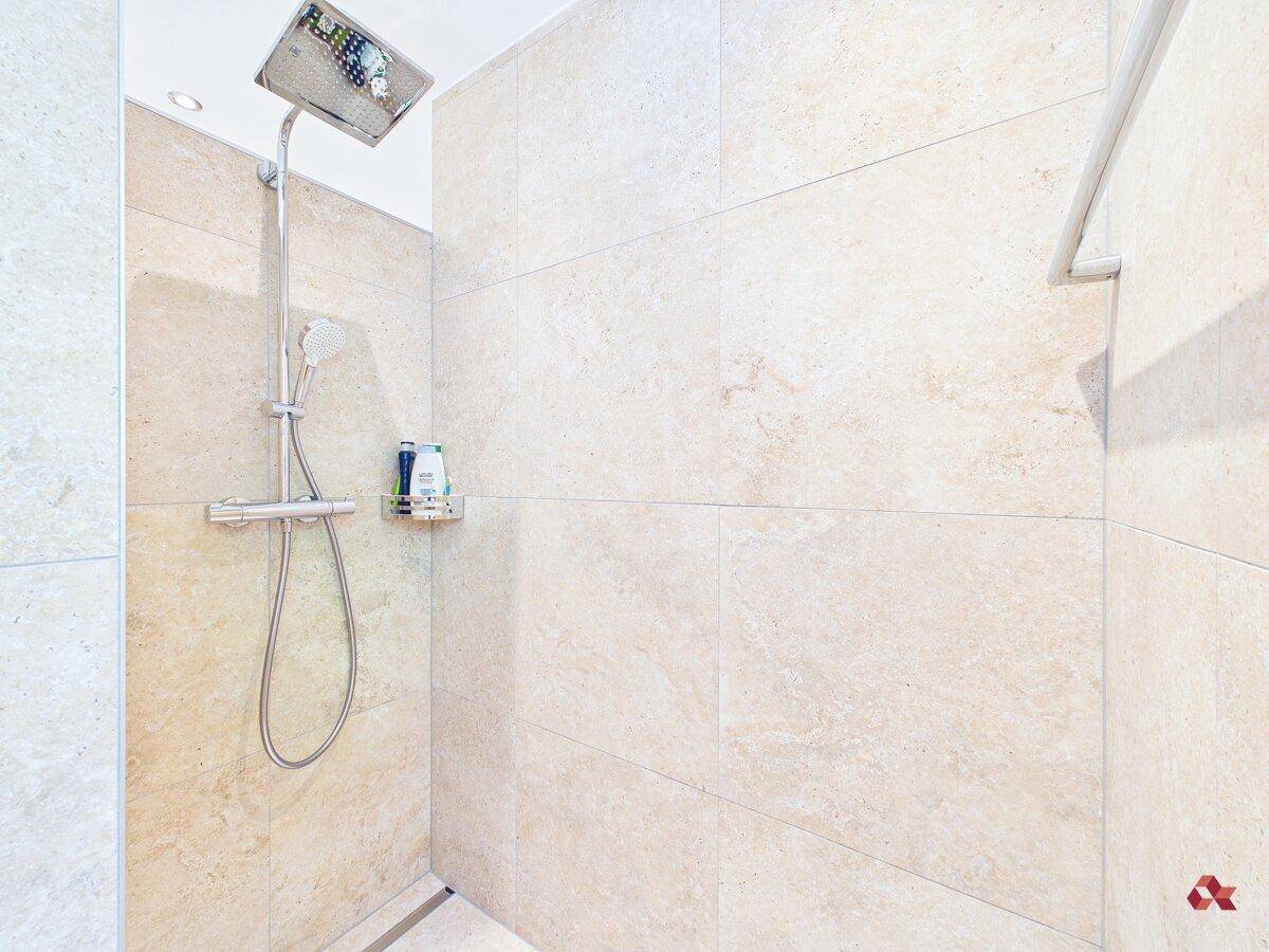 Geräumige, ebenerdige Dusche mit Regenduschkopf und beigen Fliesen an den Wänden.