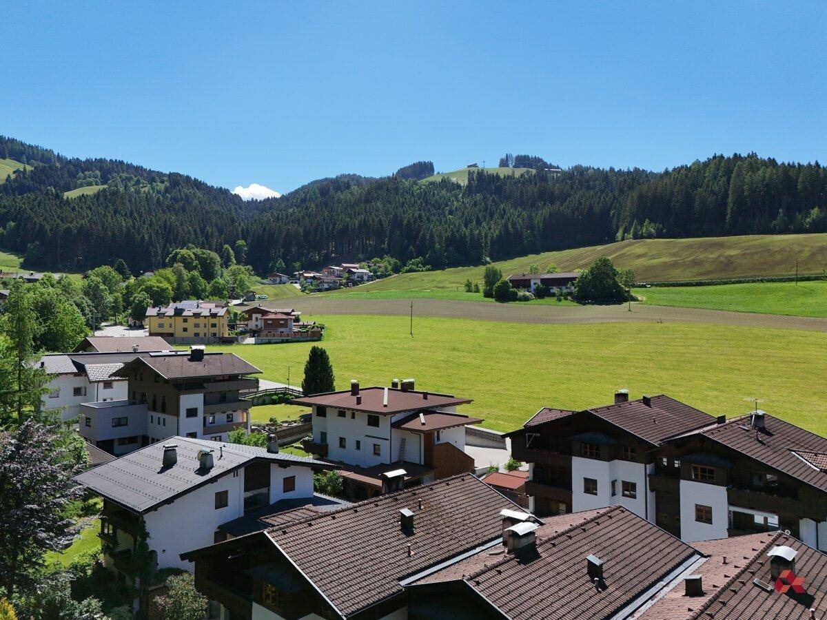 Panoramablick auf eine ländliche Wohngegend mit Bergen, grünen Feldern und Häusern.