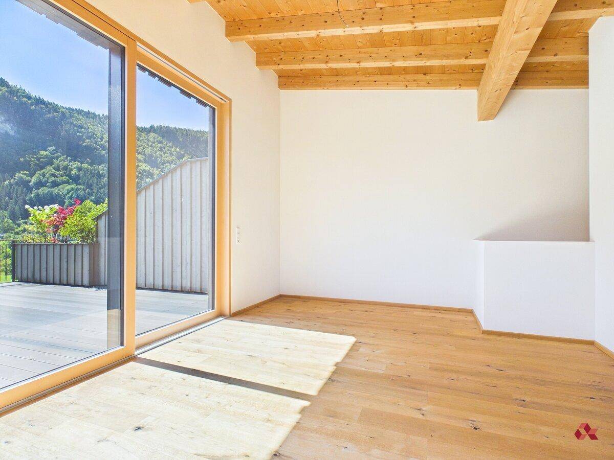 Lichtdurchfluteter Raum mit Holzbalkendecke, Parkettboden und großem Schiebefenster zur Terrasse.