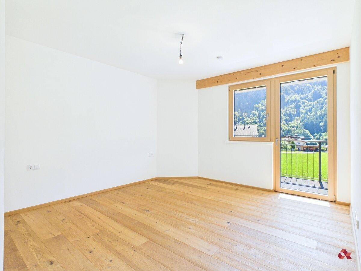 Helles, leeres Schlafzimmer mit Parkettboden und direktem Zugang zum Balkon mit Bergblick.