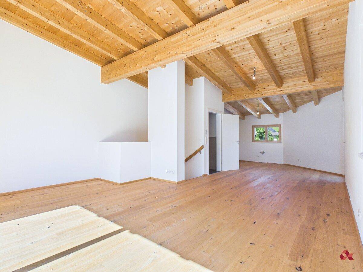 Geräumiger, leerer Raum mit sichtbaren Holzbalken und schräger Decke, ideal für offenes Wohnen.