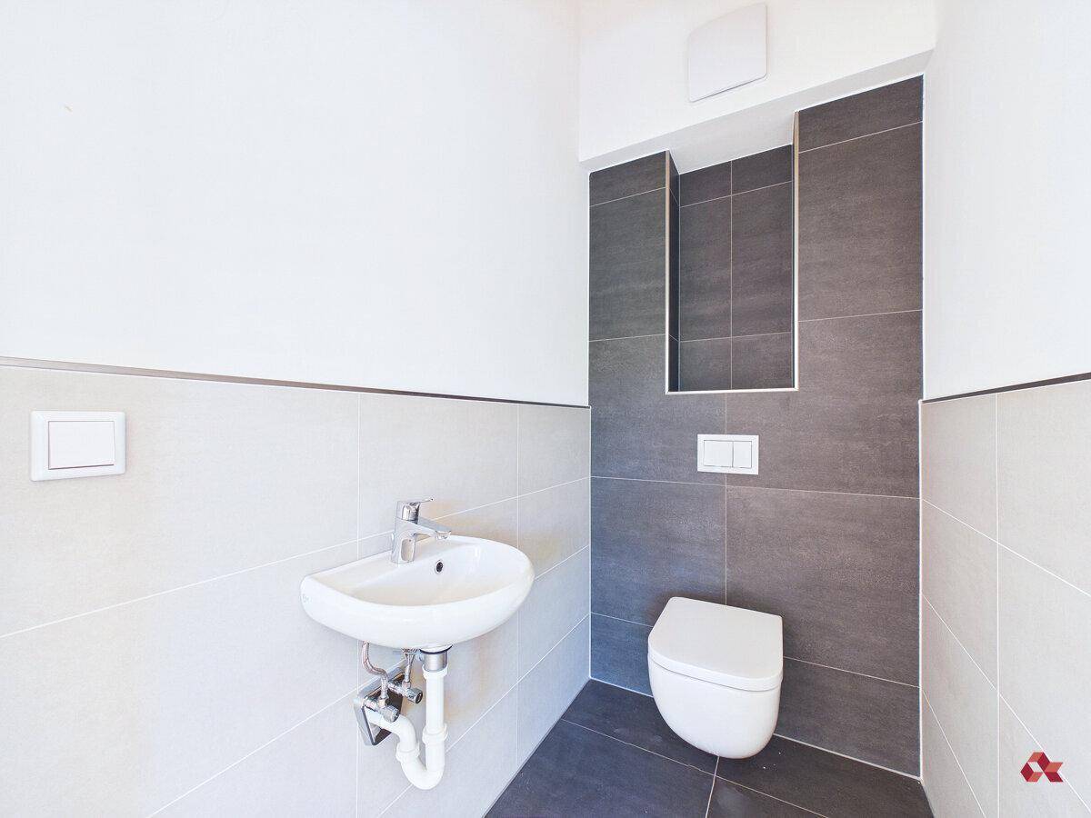 Modernes Gäste-WC mit Wand-WC, kleinem Waschbecken und grauen Fliesen.