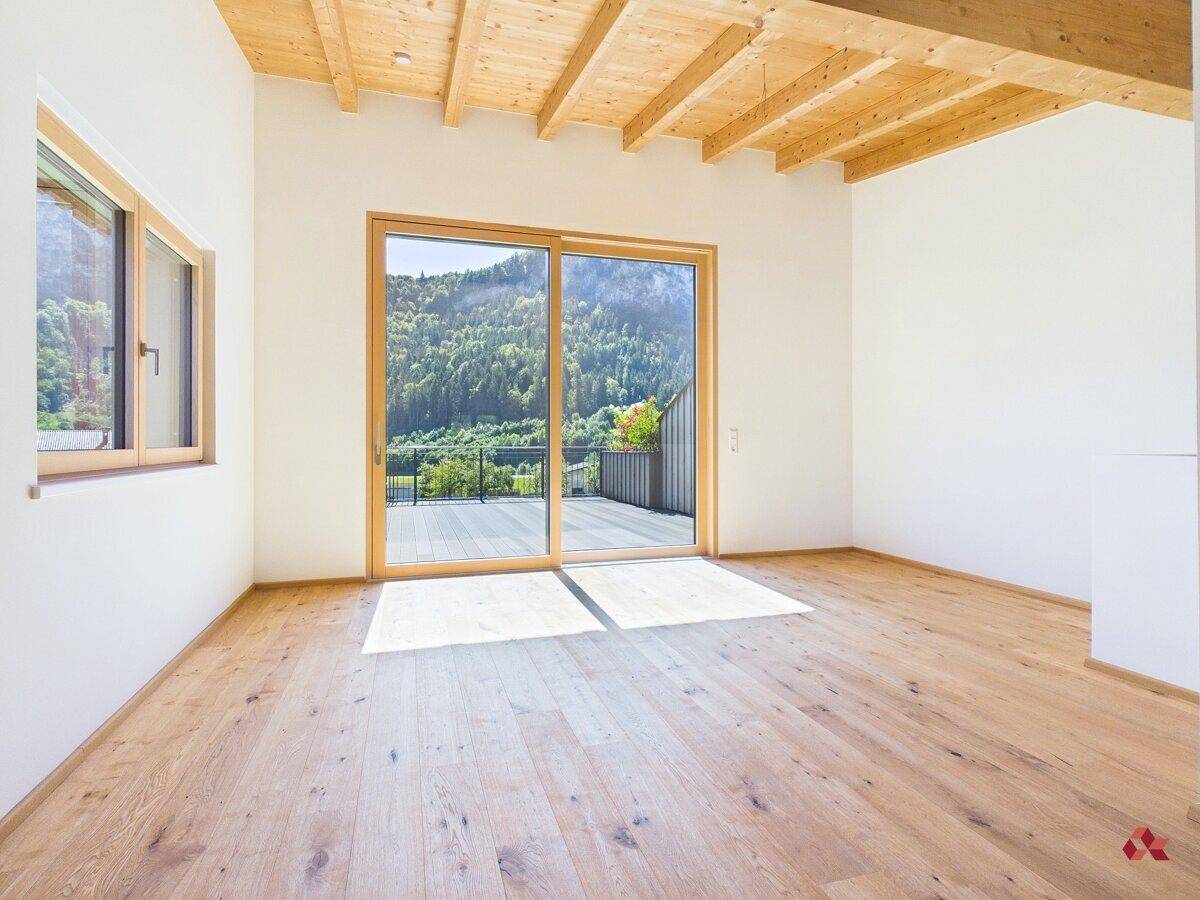 Helles, leeres Wohnzimmer mit Holzbalkendecke, Parkettboden und Zugang zur Terrasse.
