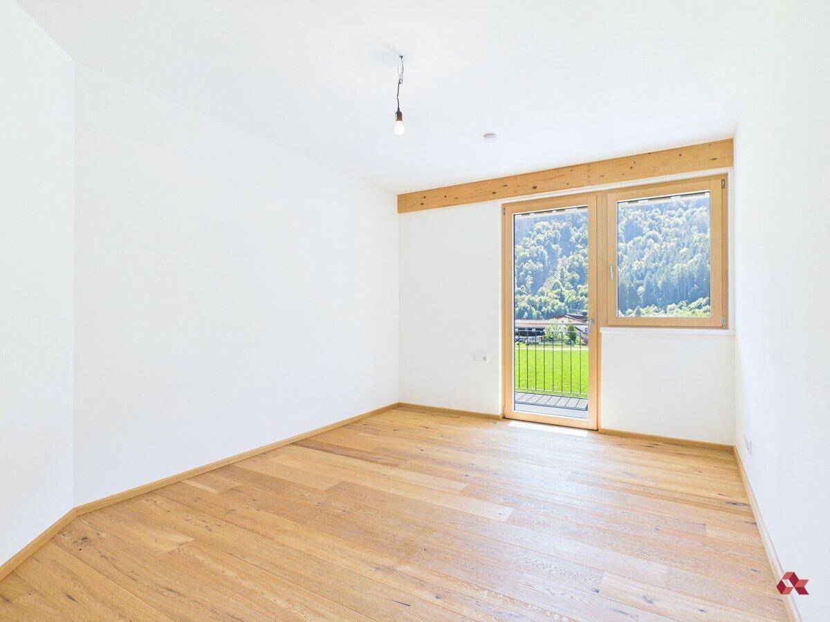 Geräumiges, leeres Schlafzimmer mit Parkettboden und Balkontür, bietet viel natürliches Licht.