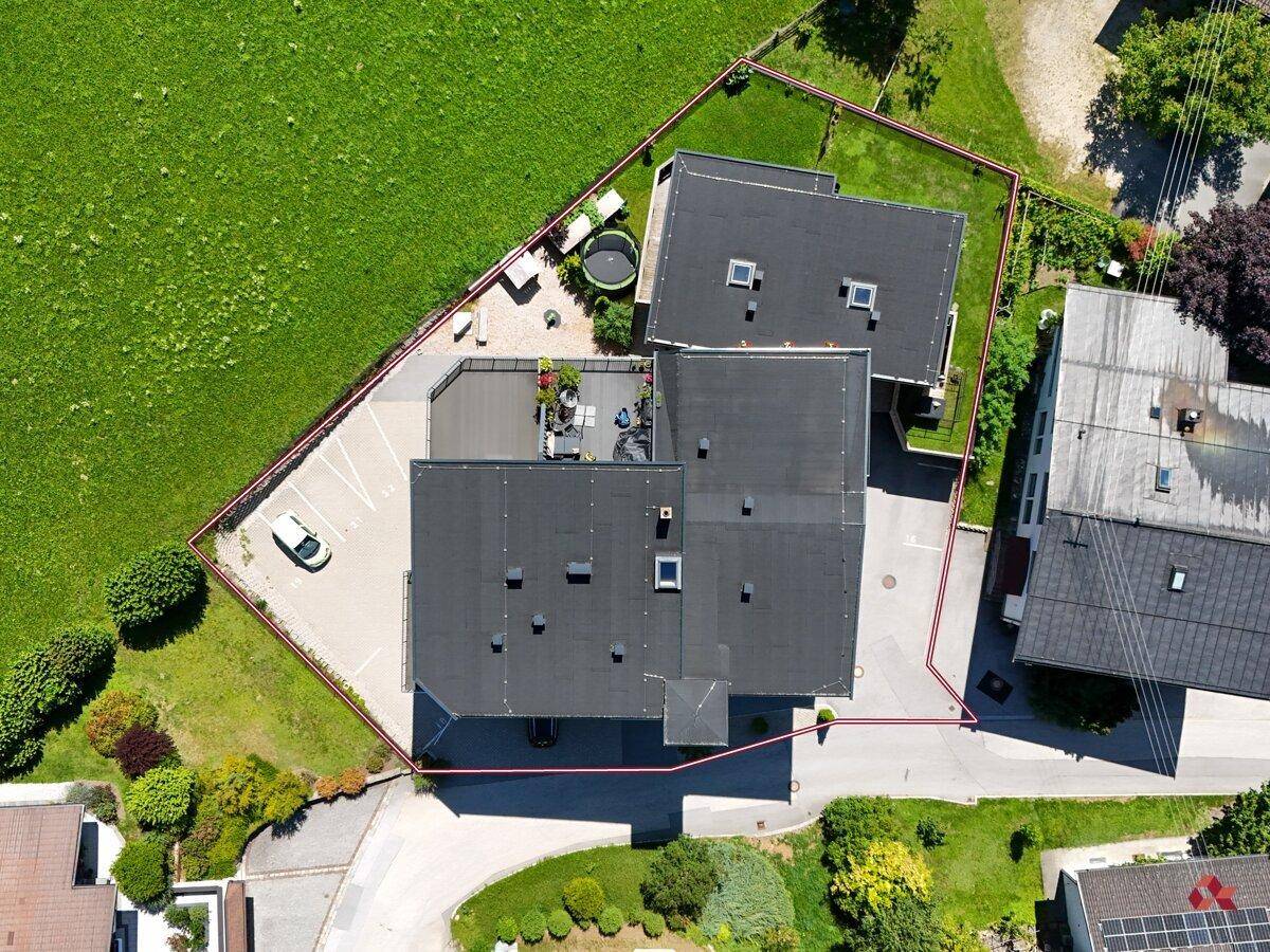 Draufsicht des Anwesens mit Gebäude, Parkplätzen und Gartenbereich, umgeben von Grünflächen.