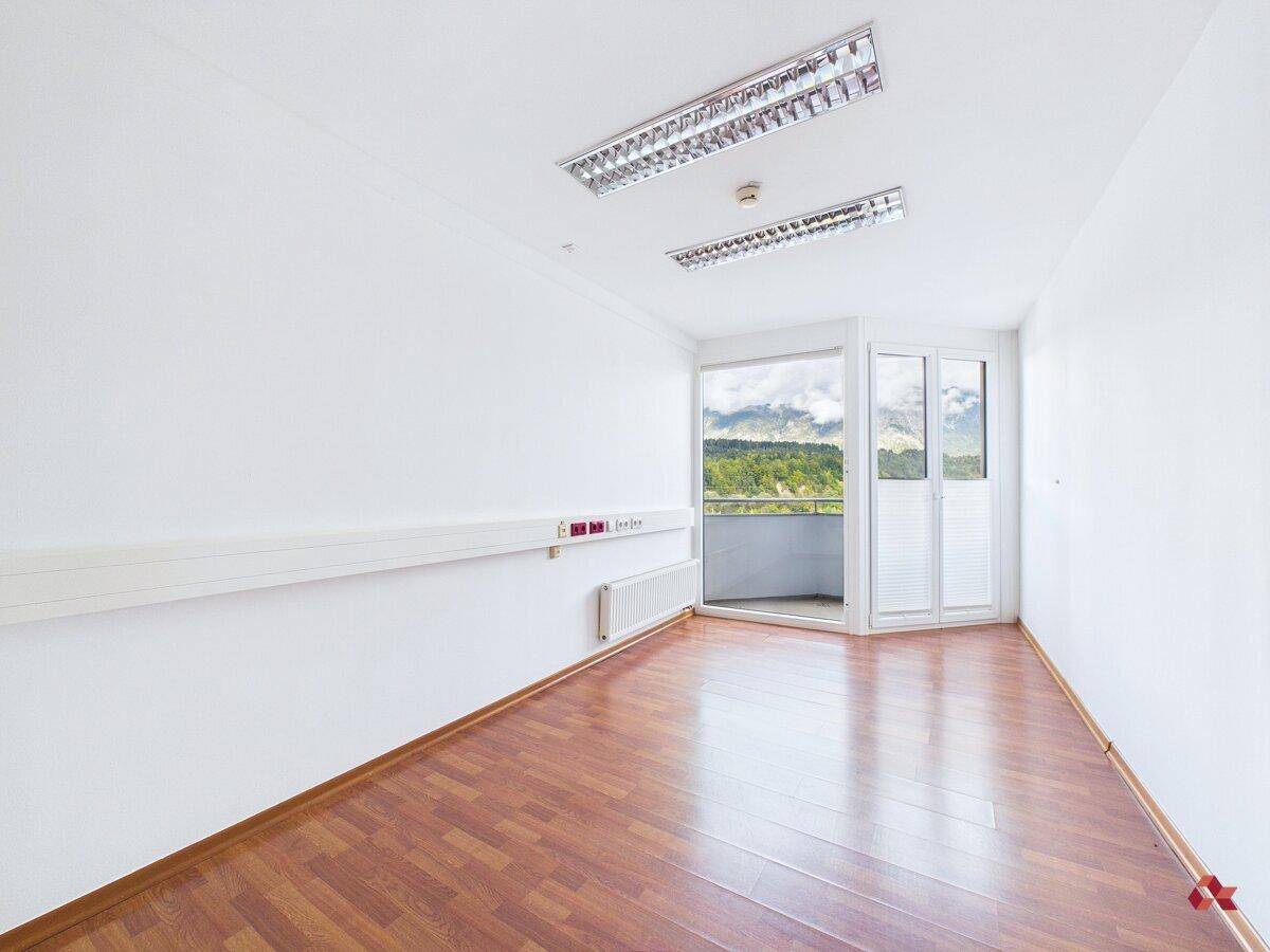 Geräumiger, heller Raum mit Holzboden, Heizkörper und Zugang zu einem kleinen Balkon.