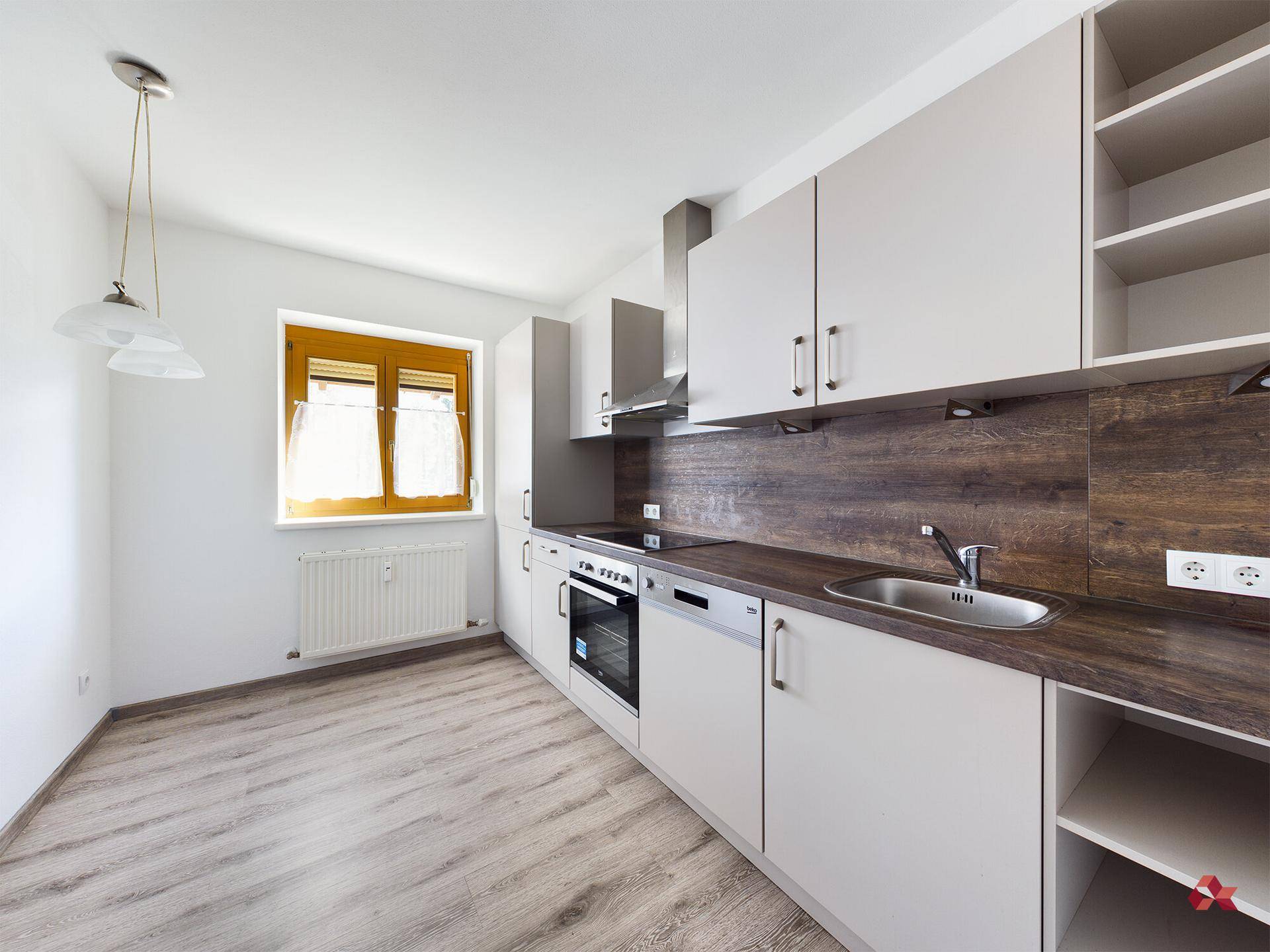 Leere Küche mit hellen Schränken, Holzoptik-Arbeitsplatte und Platz für eigene Geräte.