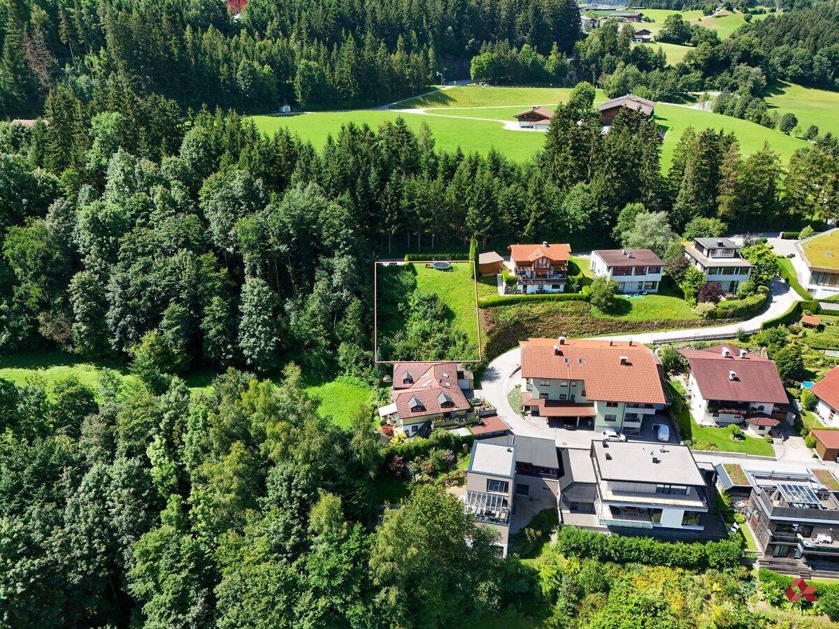 Weitläufige Luftaufnahme eines Baugrundstücks in einer ländlichen Umgebung, umgeben von Wald und Wohnhäusern.