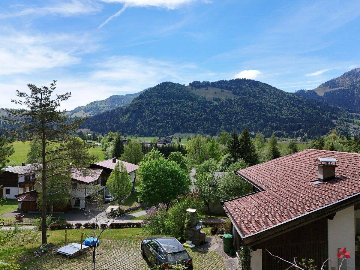 Blick über eine ländliche Wohngegend mit Häusern und grünen Hügeln im Hintergrund unter strahlend blauem Himmel.