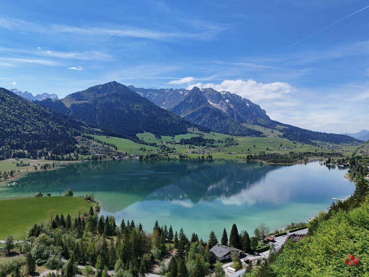 Atemberaubender Panoramablick auf einen weitläufigen See, umgeben von majestätischen Bergen und grünen Landschaften.