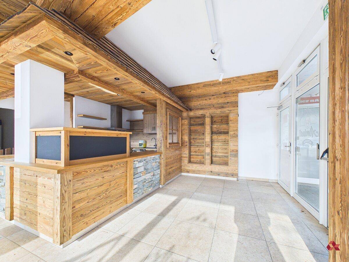 Innenbereich mit rustikalen Holz- und Steinverkleidungen, Fliesenboden und einer modernen Glastür zum Eingang.