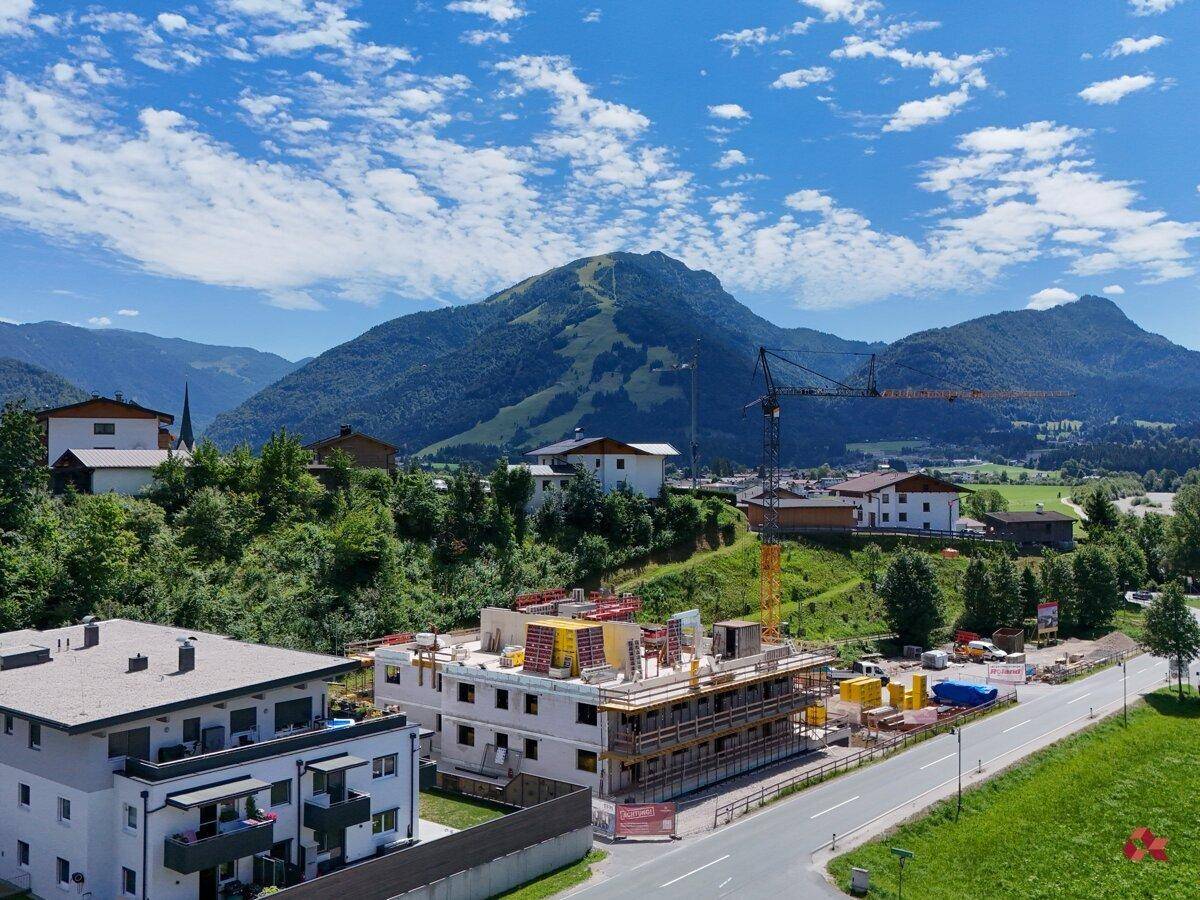 Weitläufige Luftaufnahme der Baustelle und der umliegenden Wohngegend mit Bergen im Hintergrund.