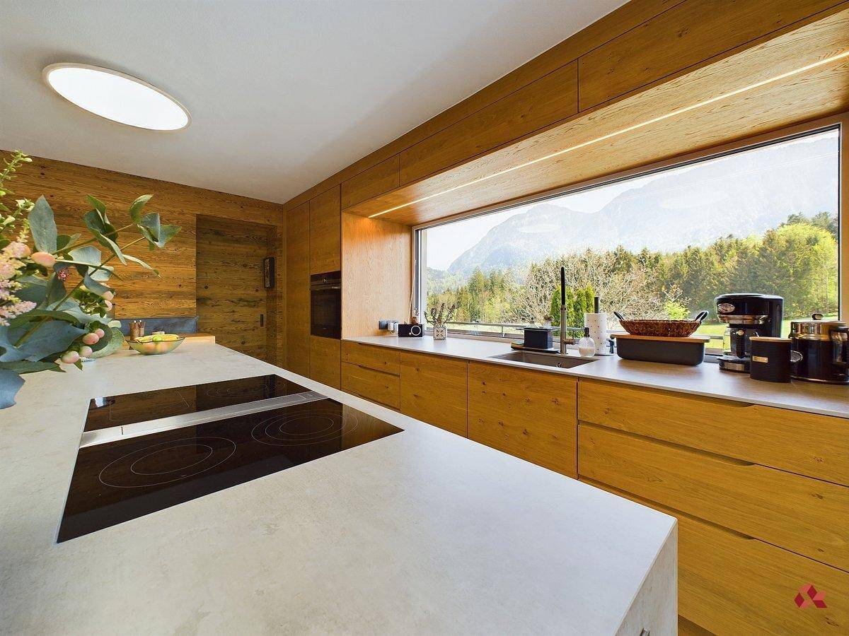 Helle Küche mit Holzfronten, Induktionskochfeld und Panoramafenster mit beeindruckendem Bergblick.