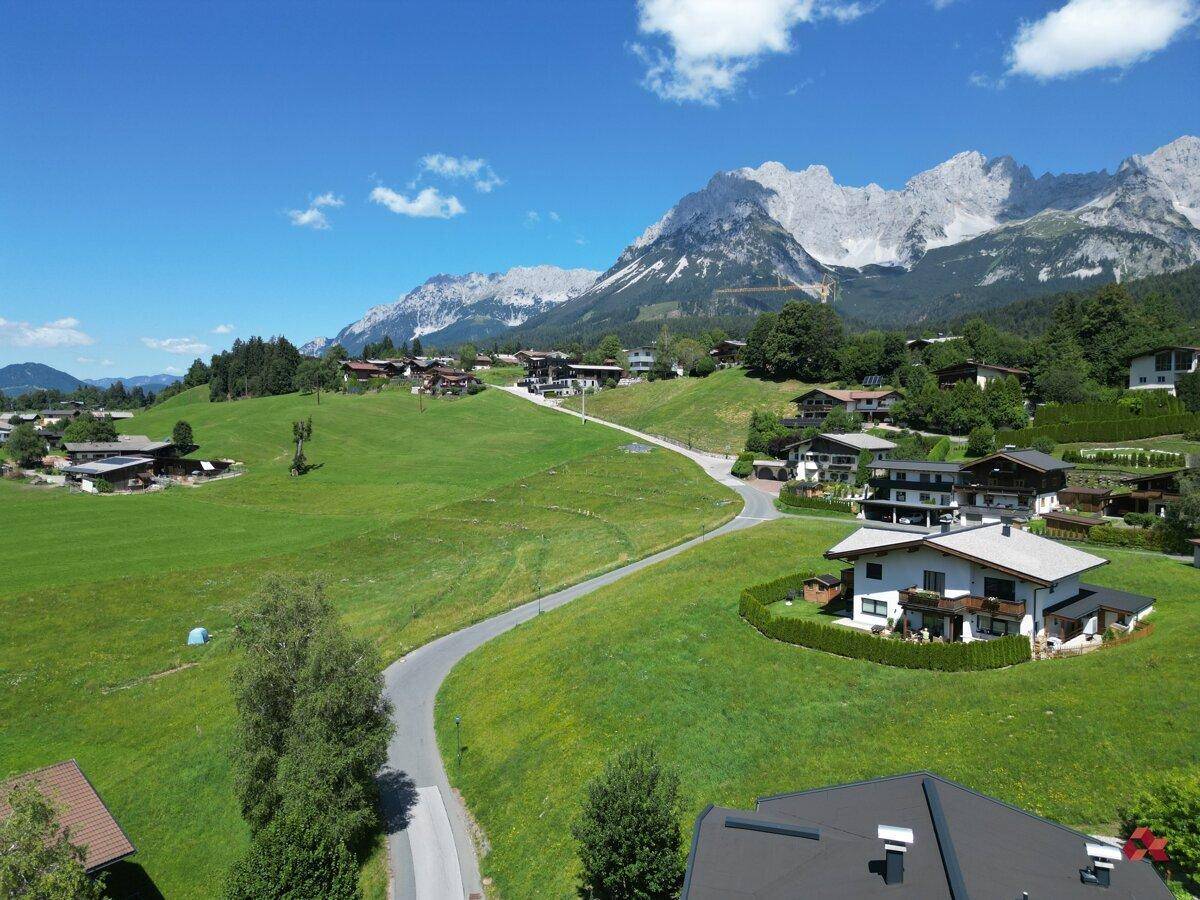 Weitläufige Landschaft mit gewundenen Straßen, Häusern und majestätischen Bergen im Hintergrund.