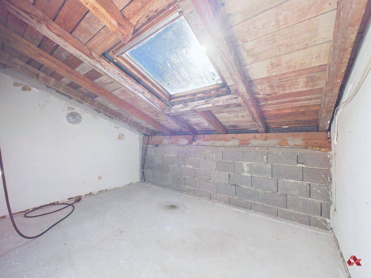 Dachbodenraum mit sichtbaren Holzbalken, Dachschräge und einem Dachfenster.