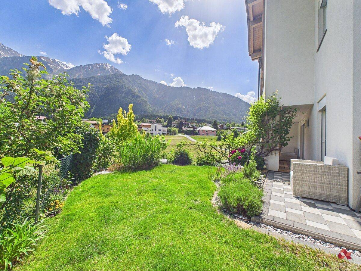 Gepflegter Garten mit Rasenfläche, Terrasse und beeindruckendem Bergblick.