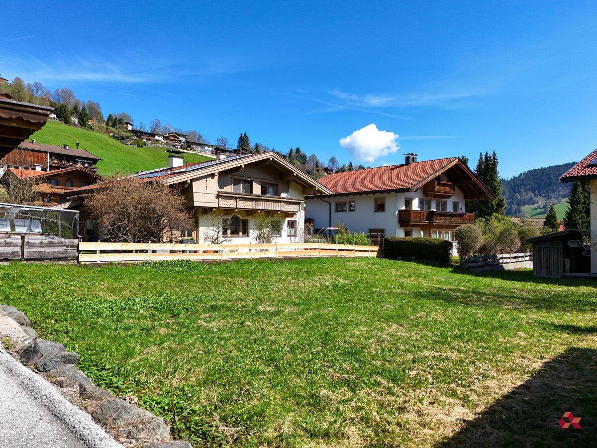 Häuser in einer ländlichen Siedlung mit grünen Wiesen und Bergen im Hintergrund.