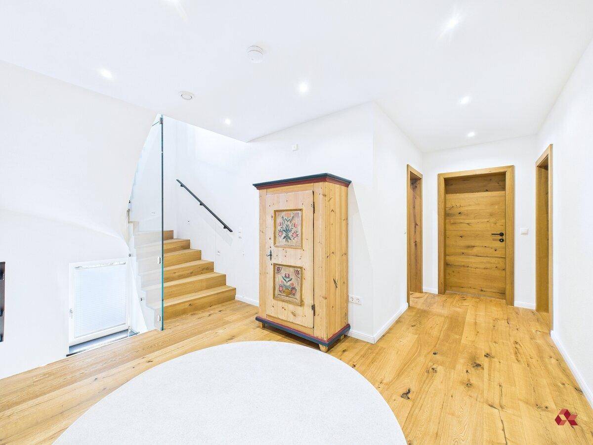 Heller Flur mit Holztreppe, Glasgeländer und traditionellem Schrank.