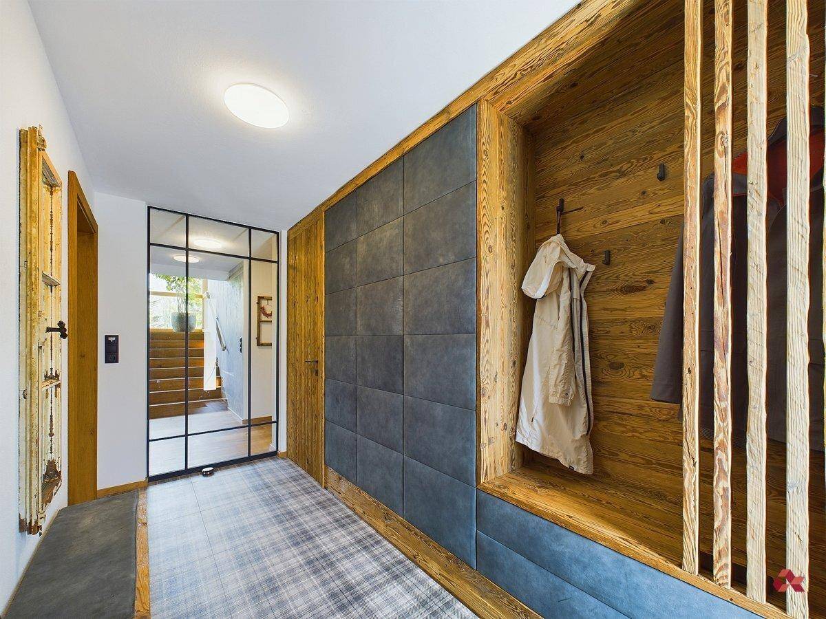 Moderner Eingangsbereich mit Holzwänden, integrierter Garderobe und stilvoller Glastür zum Treppenhaus.
