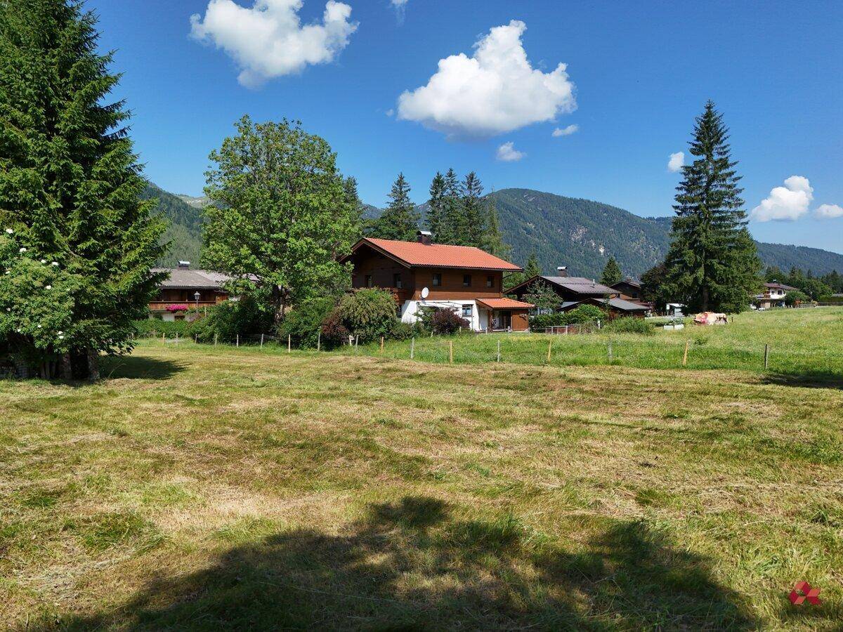 Weite grüne Fläche mit traditionellen Häusern und üppiger Vegetation in den Bergen.