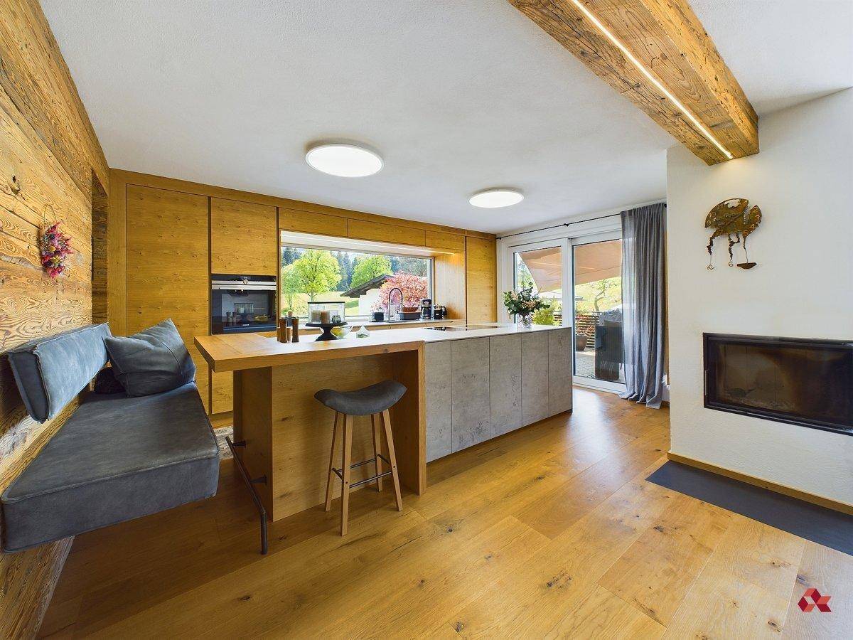 Moderne offene Küche mit Holzschränken, Kücheninsel und integriertem Kamin im Wohnbereich.