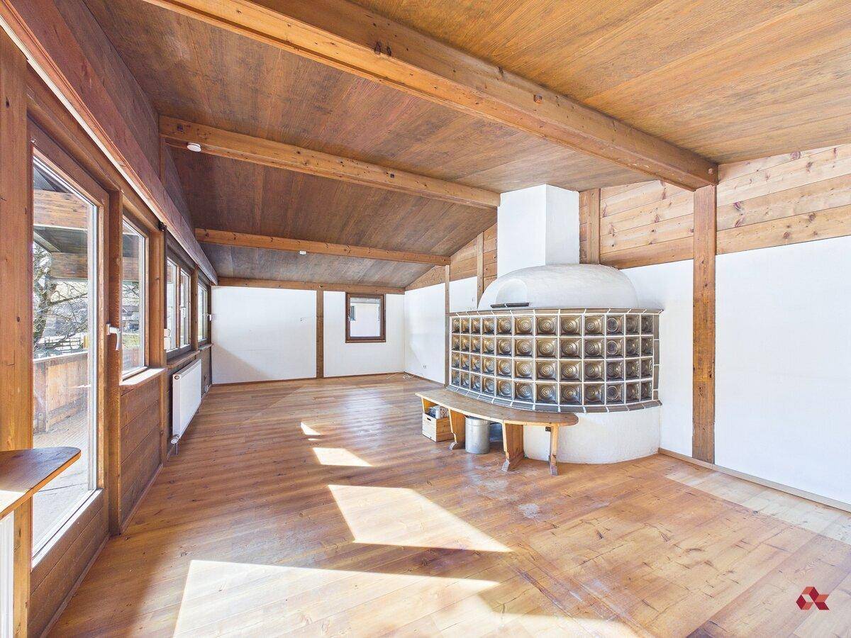 Großzügiges Wohnzimmer mit traditionellem Kachelofen, Holzboden und vielen Fenstern.