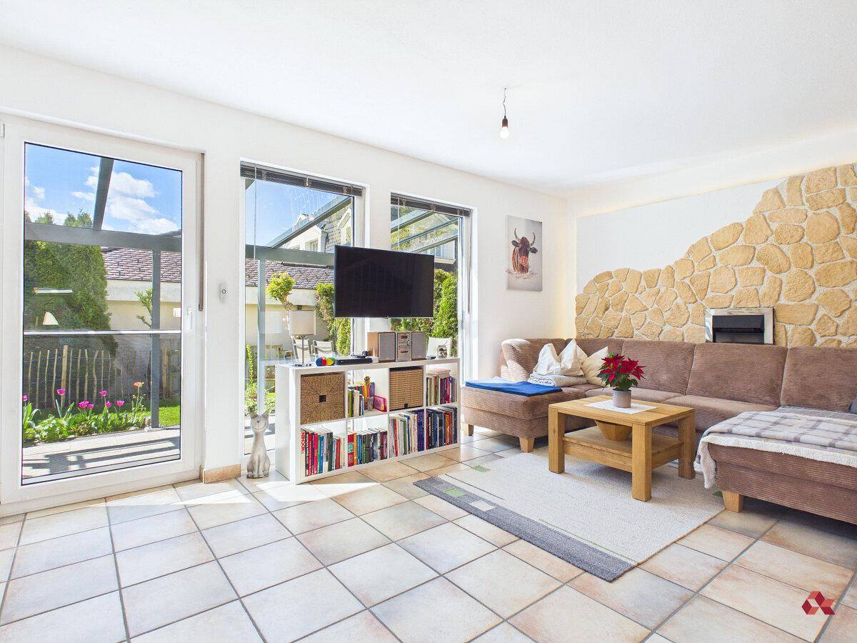 Helles Wohnzimmer mit Fliesenboden, gemütlichem Sofa und Zugang zur Terrasse.