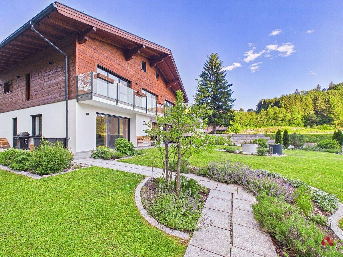Seitlicher Blick auf das moderne Haus mit Holzfassade und einem liebevoll angelegten Gartenweg.