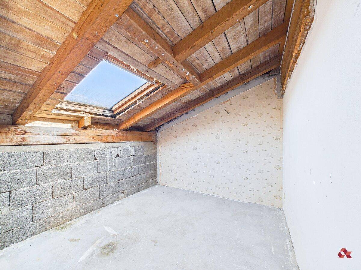Dachbodenraum mit sichtbaren Holzbalken, Dachschräge und einem Dachfenster.