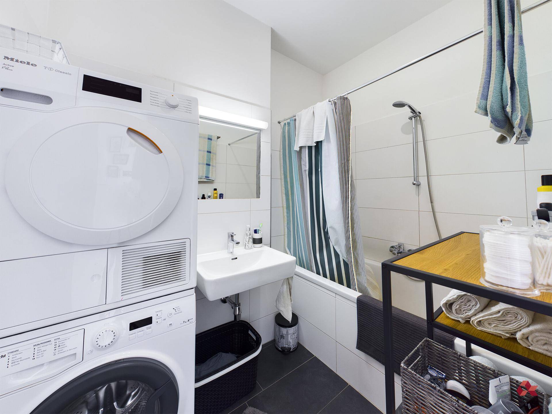Funktionales Badezimmer mit Badewanne, Waschbecken und integrierter Waschmaschine sowie Trockner.