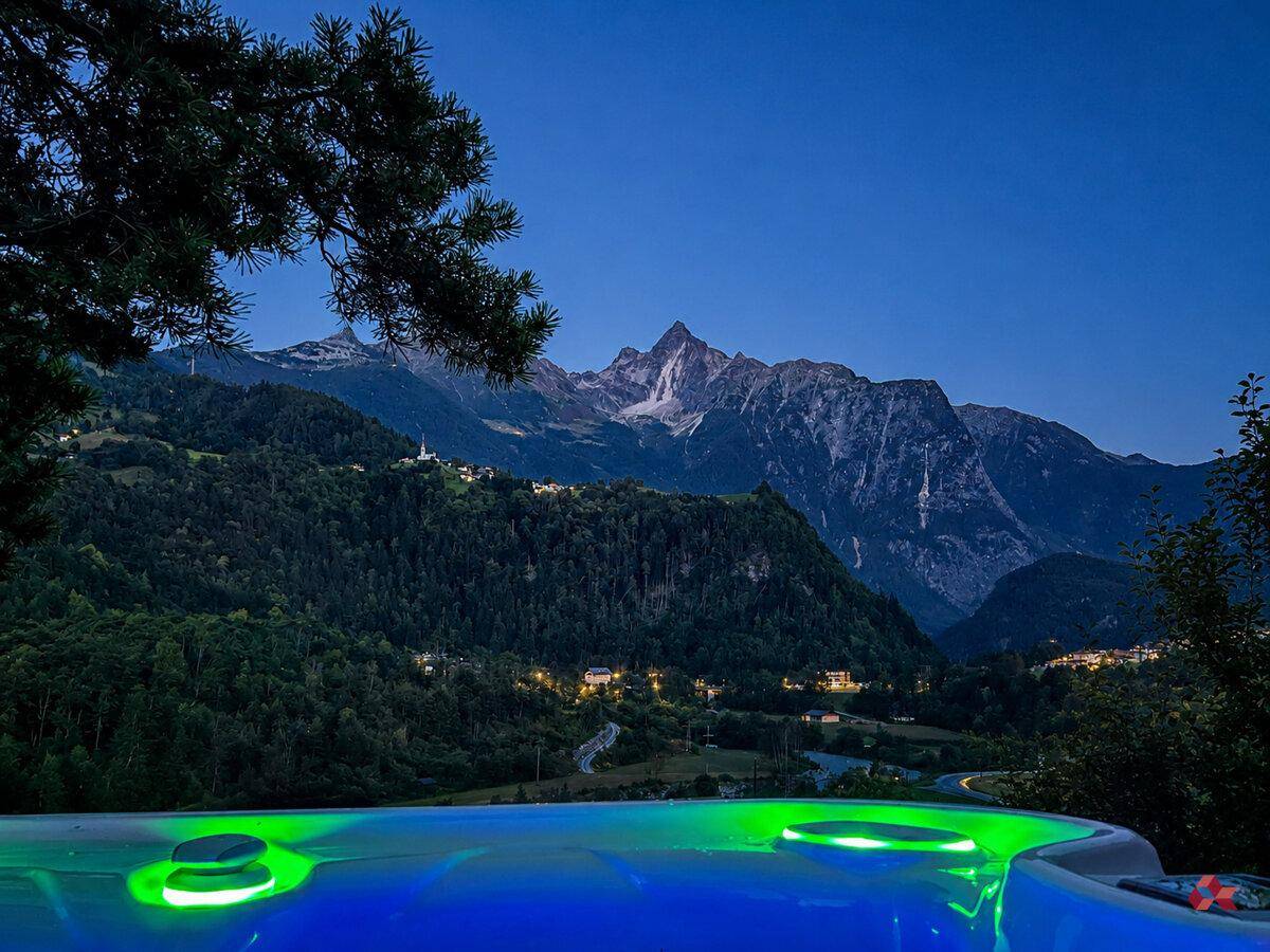 Beleuchteter Whirlpool bei Nacht mit malerischem Blick auf die beleuchteten Berge.