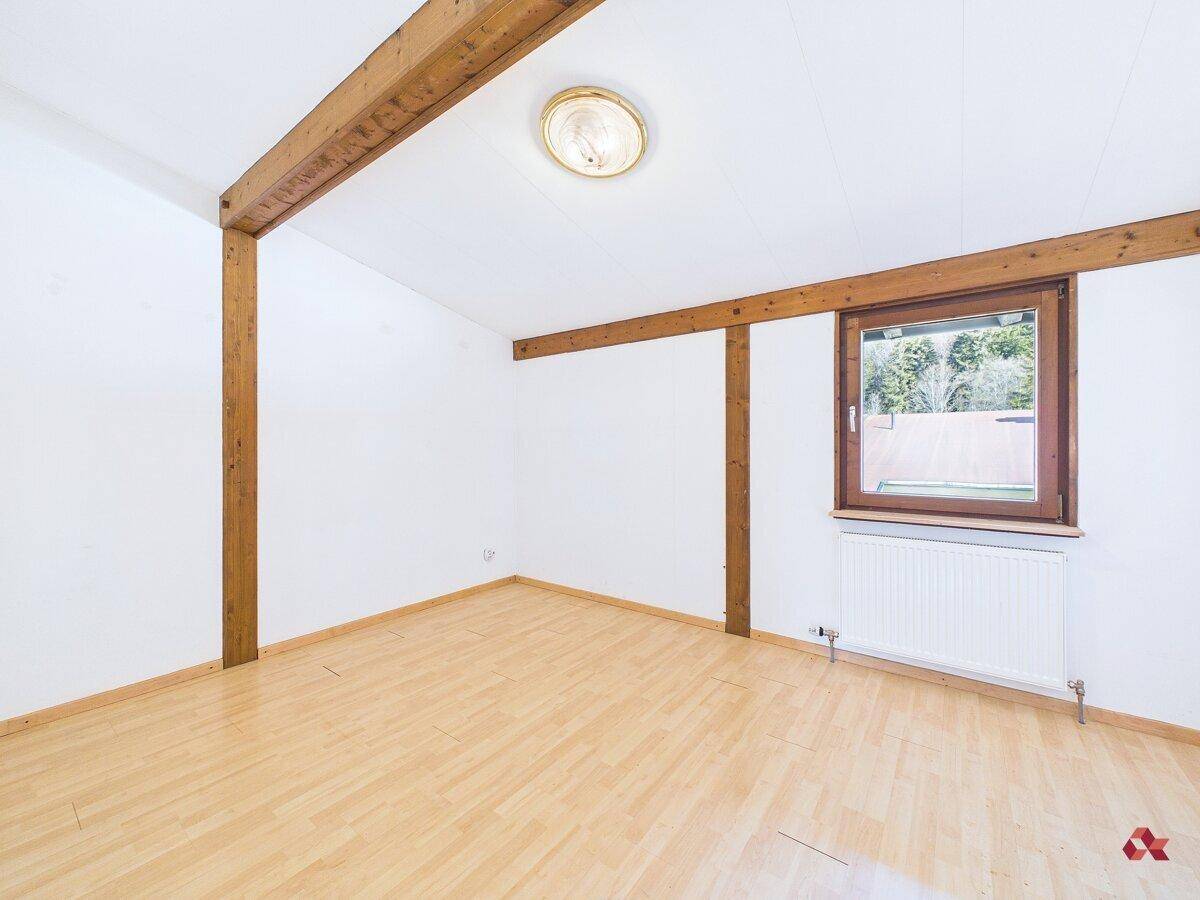 Geräumiges Schlafzimmer mit Holzbalken und Parkettboden, bietet viel Licht und alpines Flair.