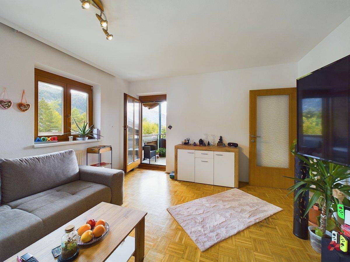 Helles Wohnzimmer mit Parkettboden, bequemer Couch und Zugang zum Balkon mit Bergblick.