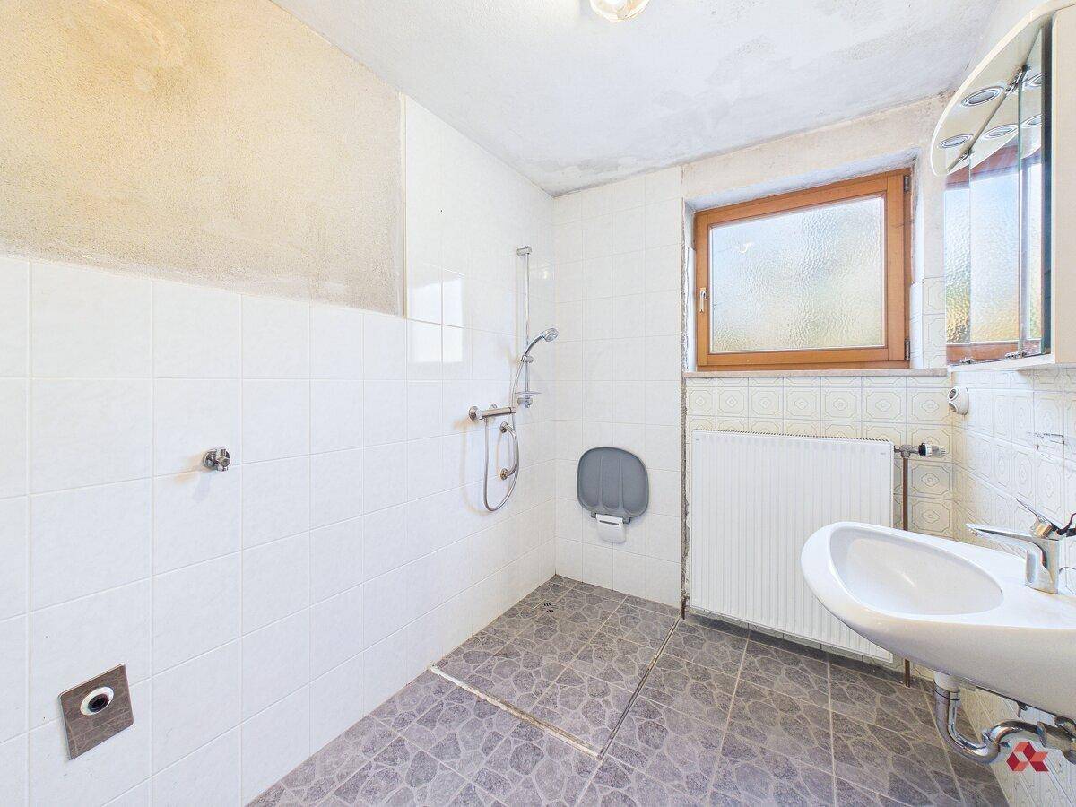 Badezimmer mit Dusche, Waschbecken, Fenster und weißen Wandfliesen.