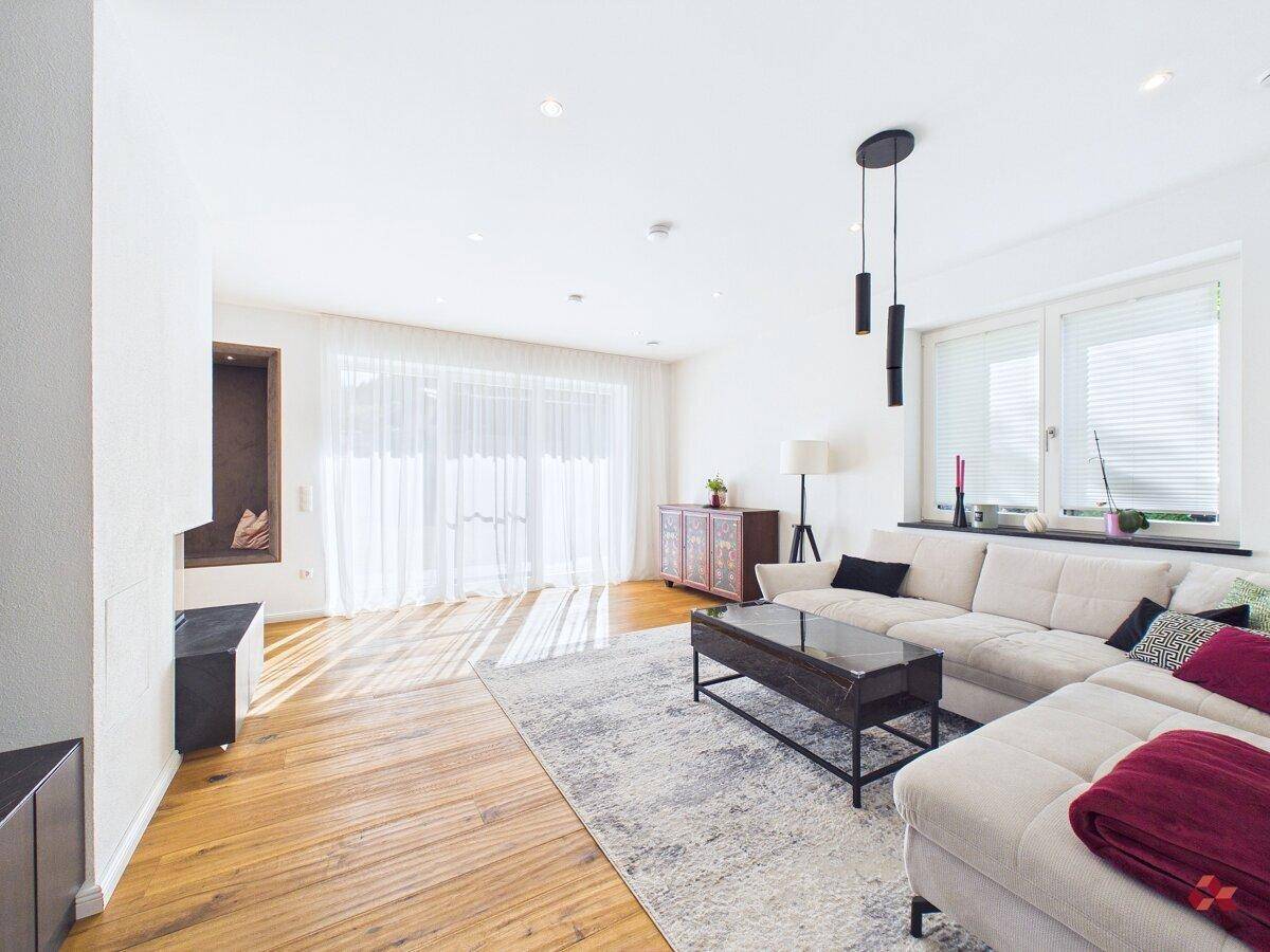 Geräumiges Wohnzimmer mit hellem Sofa, Holzboden und großen Fenstern.